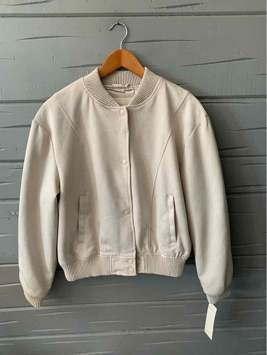 Tan long-sleeve bomber jacket with ribbed collar, cuffs, and hem hanging on wooden hanger.