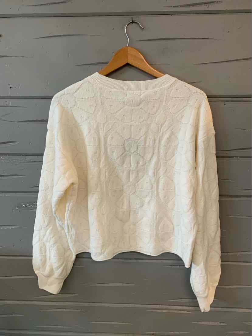 White long-sleeve knit sweater with floral cable patterns and ribbed cuffs, displayed on wooden hanger.