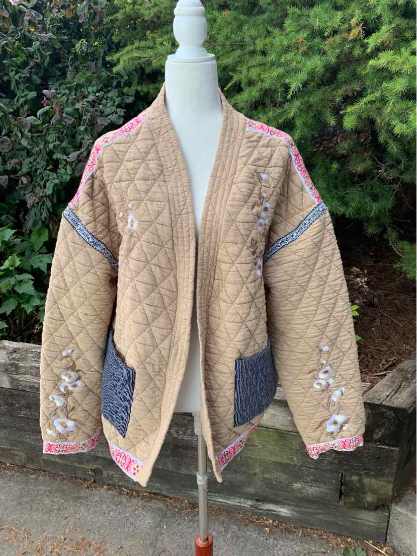 Tan quilted oversized jacket with floral embroidery and contrasting dark gray inner pockets.