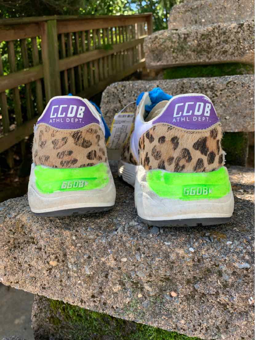 Multi-colored low-top sneakers with leopard print on heels, purple fabric tabs, and neon green accents on worn soles.