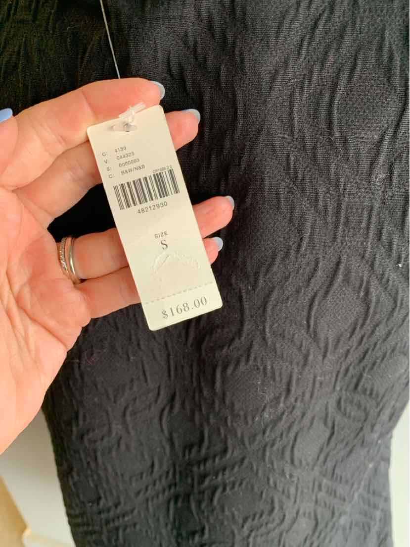 Black textured fabric dress tag displaying price and size small details held by hand with light pink nails and rings.