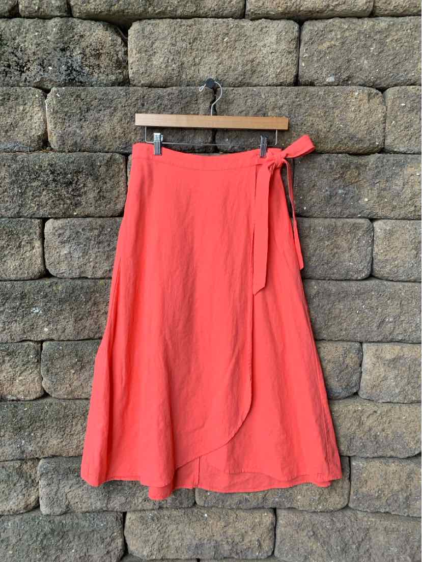 Coral midi wrap skirt with tie waist and flowing A-line silhouette hanging on wooden hanger.