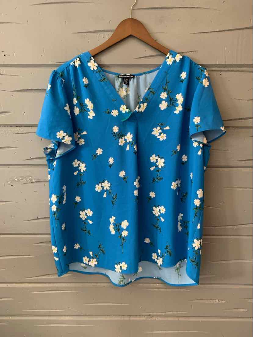 Blue short-sleeve blouse with white floral print and V-neck on wooden hanger.