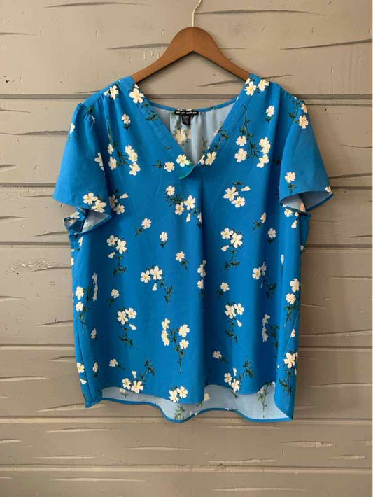 Blue short-sleeve blouse with white floral print and V-neck on wooden hanger.