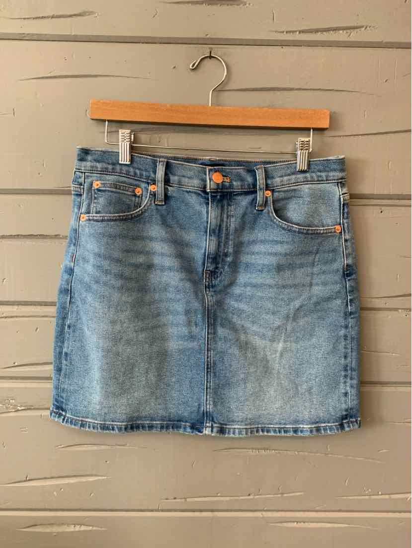Light blue denim mini skirt with front pockets, button closure, and subtle fading details.