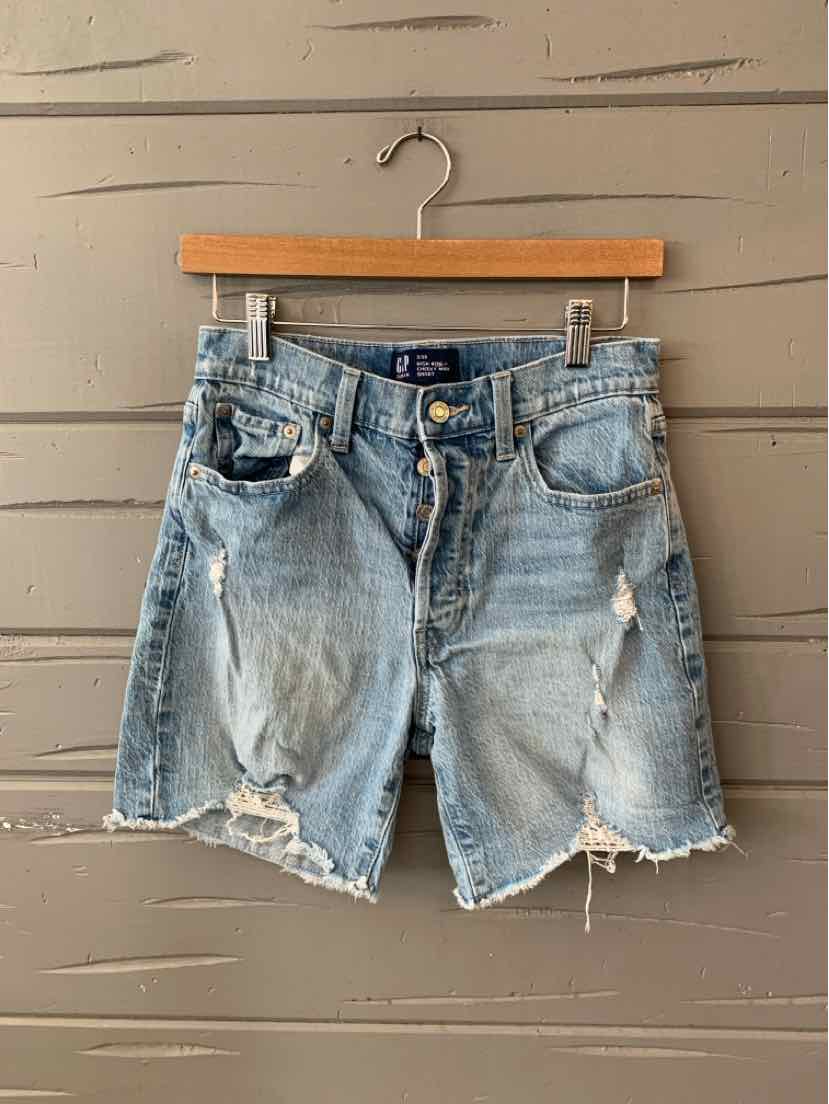 Light blue distressed denim shorts with frayed hems and multiple pockets hanging on wooden hanger.