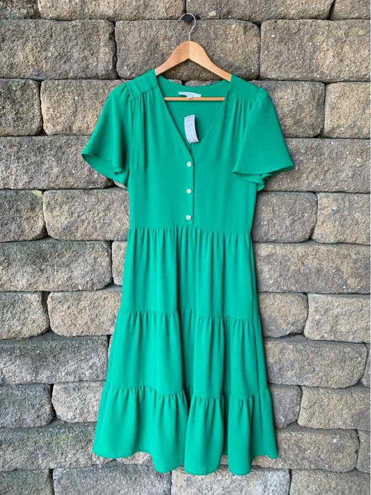 Green short-sleeve midi dress with buttons down front and tiered skirt on wooden hanger.