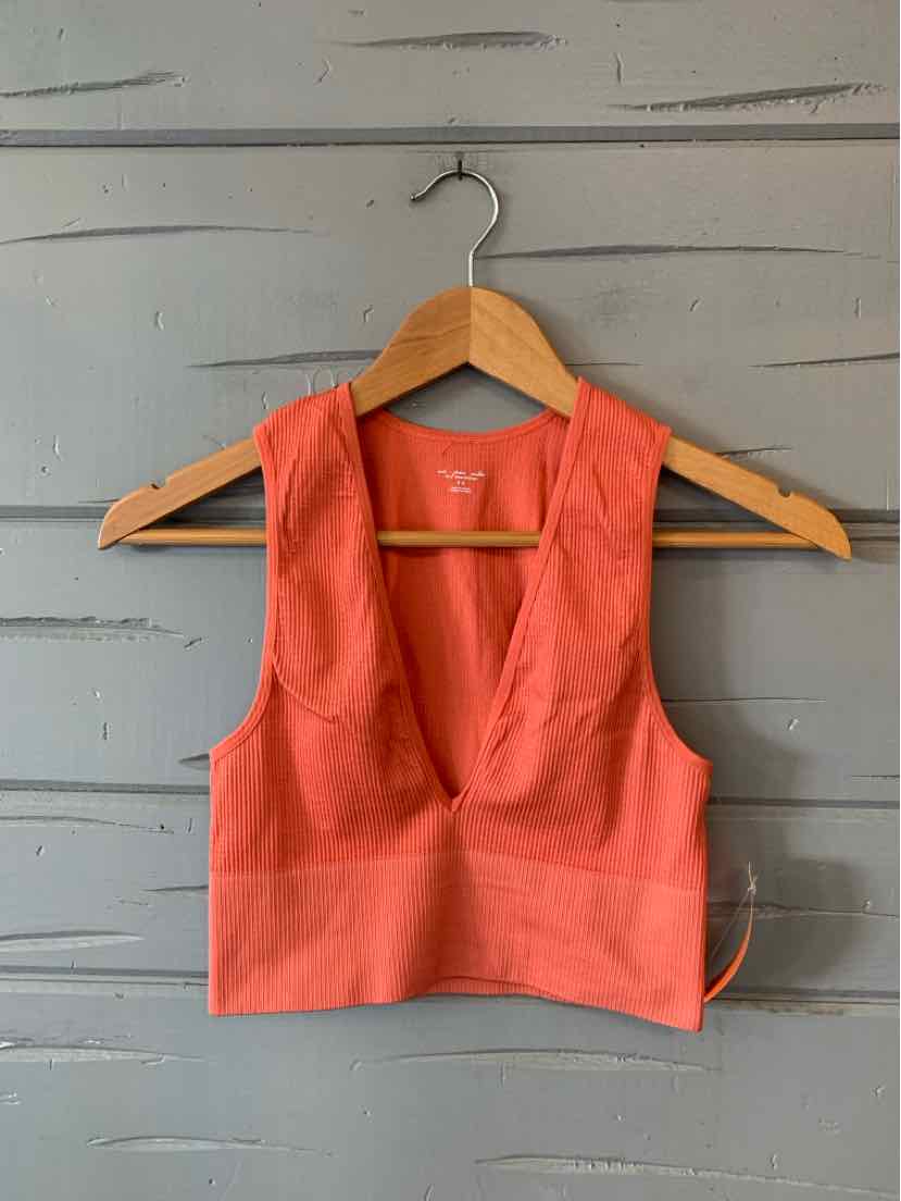 Coral sleeveless crop top with deep scoop neck and fitted band on wooden hanger against gray wall.