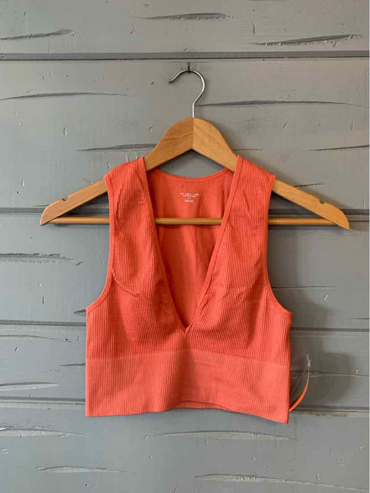Coral sleeveless crop top with deep scoop neck and fitted band on wooden hanger against gray wall.