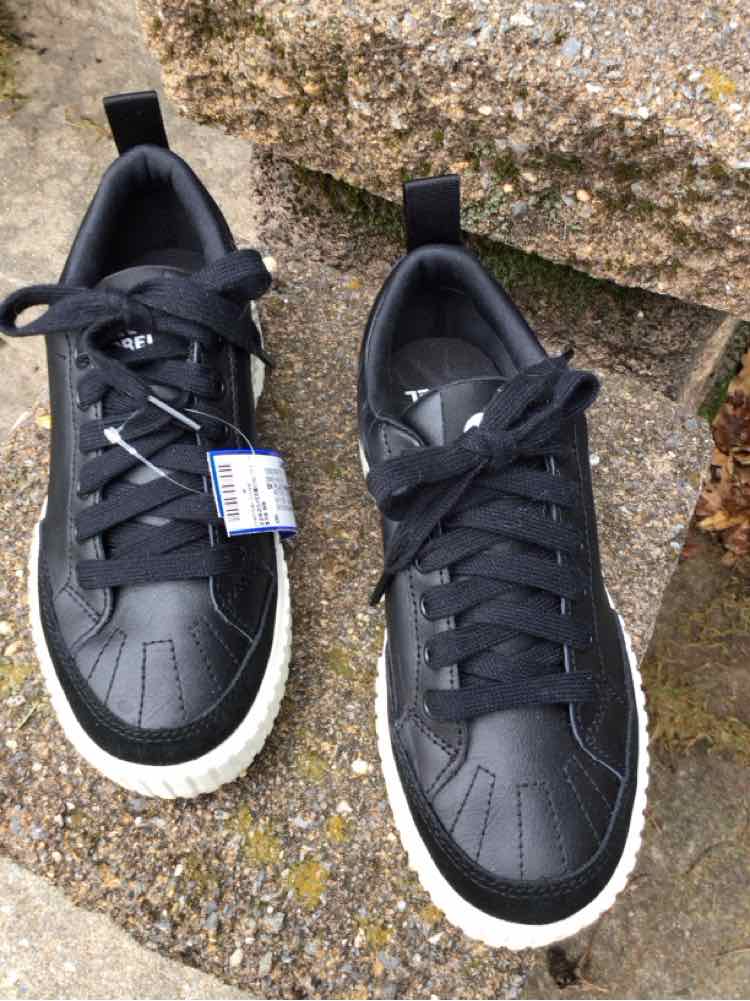 Black leather sneakers with white rubber soles and black laces on stone steps.