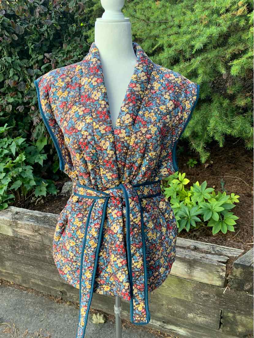 Sleeveless floral vest with multicolor blossoms and fabric belt cinching the waist.