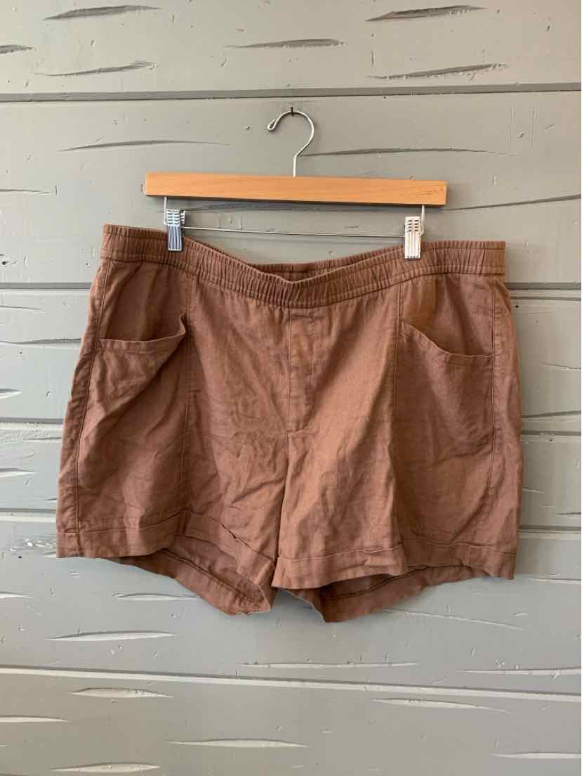 Brown solid casual shorts with front pockets, size XL, hanging on wooden hanger against textured wall.