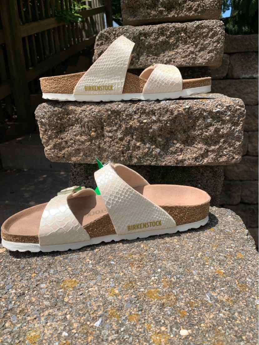 White textured leather Birkenstock sandals with two adjustable straps and cork footbed on stone background.