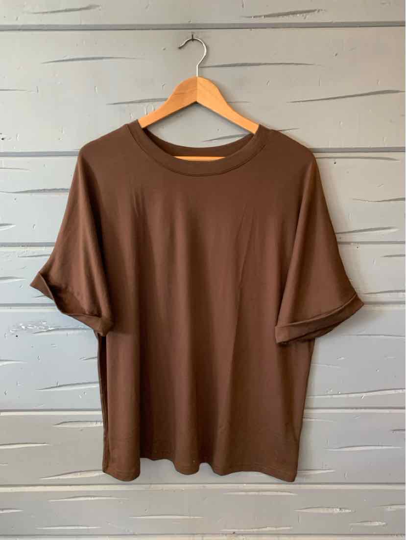 Brown short-sleeve crewneck t-shirt in medium size hanging on wooden hanger against gray wooden wall.