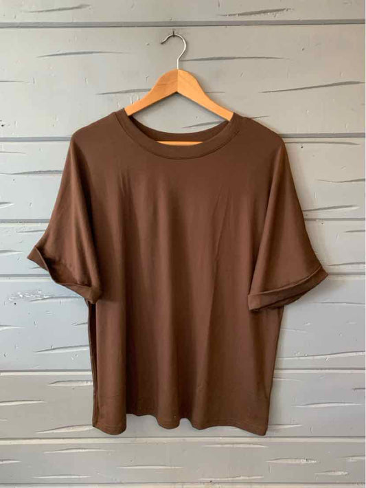 Brown short-sleeve crewneck t-shirt in medium size hanging on wooden hanger against gray wooden wall.
