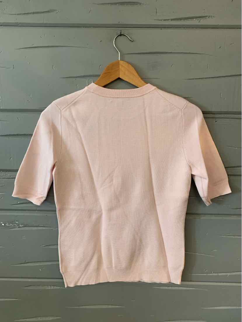 Light pink short-sleeve knit top with crew neckline hanging on wooden hanger against gray wood panel background.