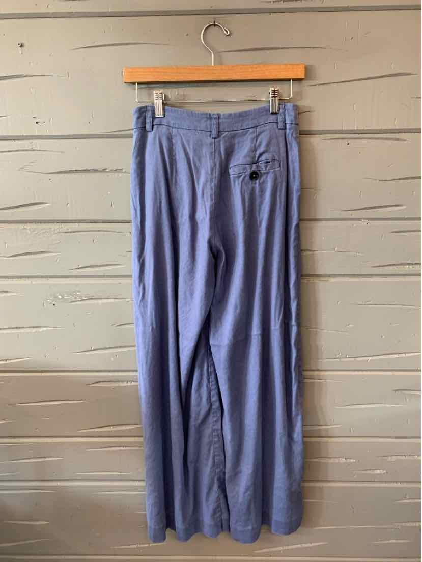 Blue wide-leg pants with high waist and buttoned back pocket, hanging on wooden hanger.