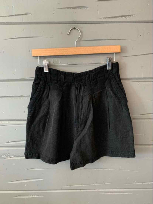Black high-waisted shorts with front pleats and an elastic waistband hanging on wooden hanger.