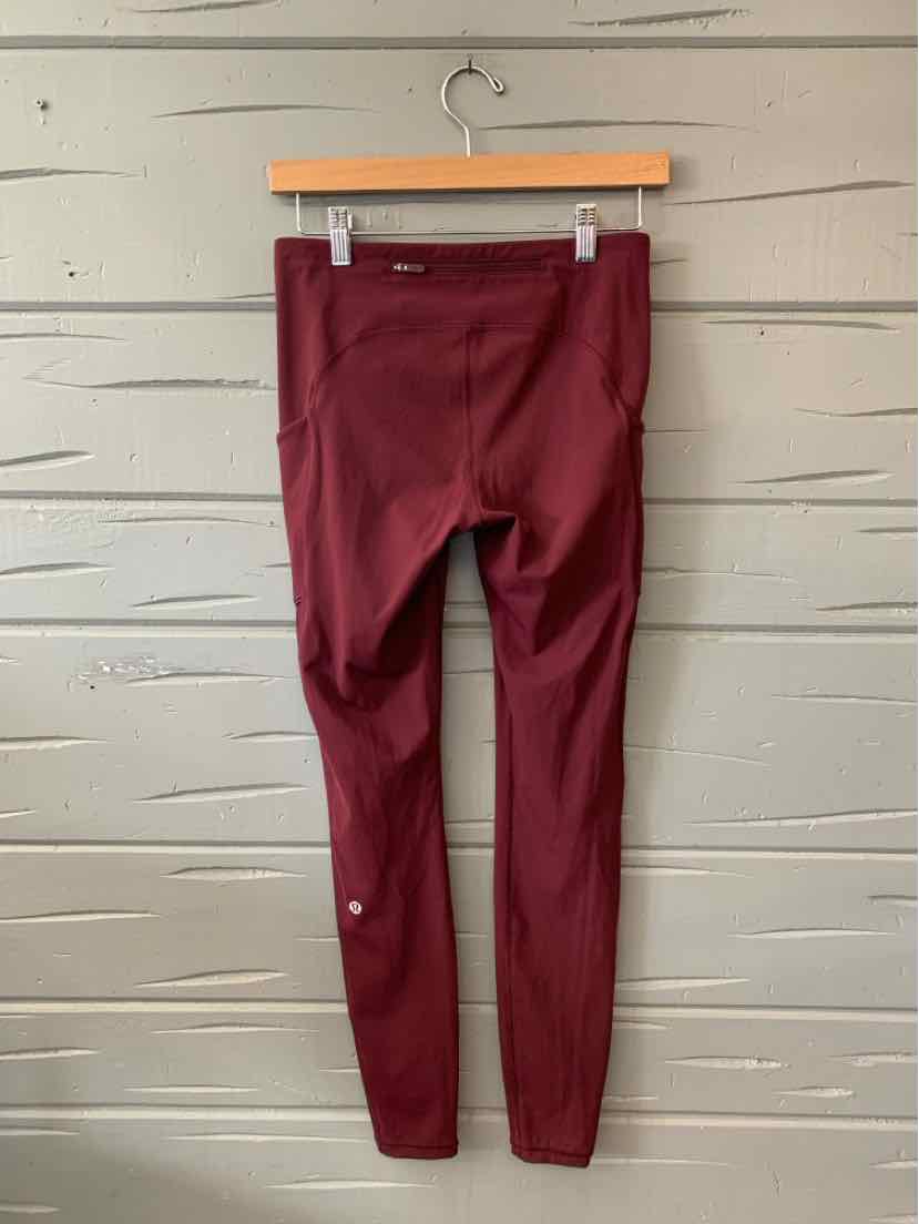 Burgundy high-waisted leggings with a smooth, stretchy fabric and a slim fit, hanging on a wooden hanger.