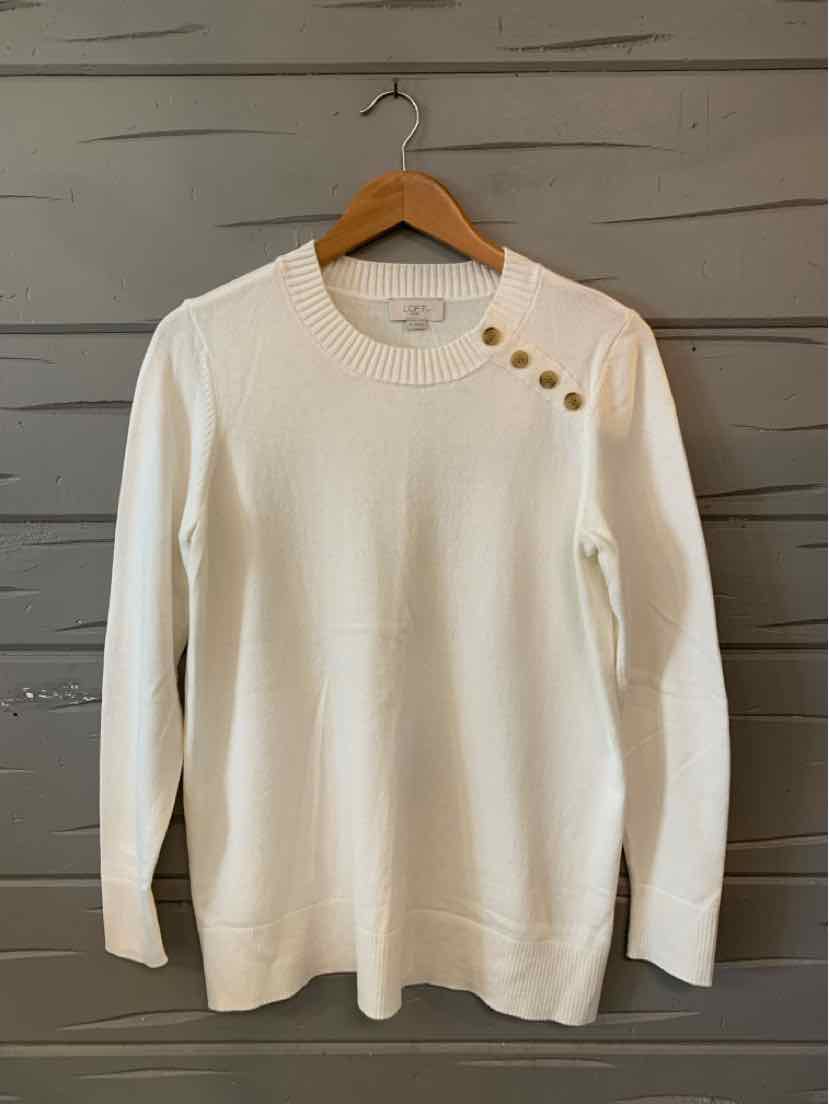 White long-sleeve knit sweater with three brown buttons near the left shoulder, crew neckline.