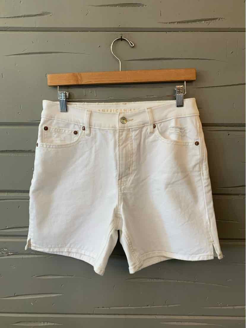 White denim shorts with front and back pockets, button closure, and belt loops hanging on wooden hanger.