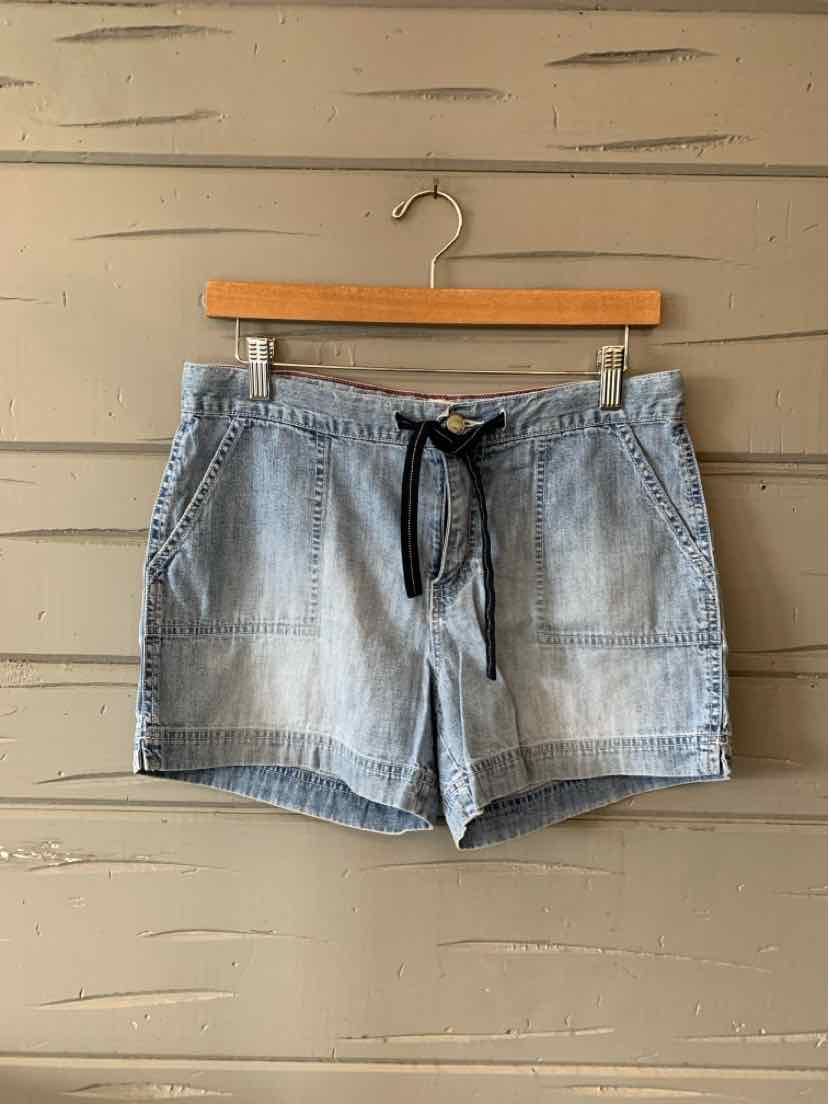 Light blue denim shorts with a black drawstring waist and front pockets hanging on a wooden hanger.