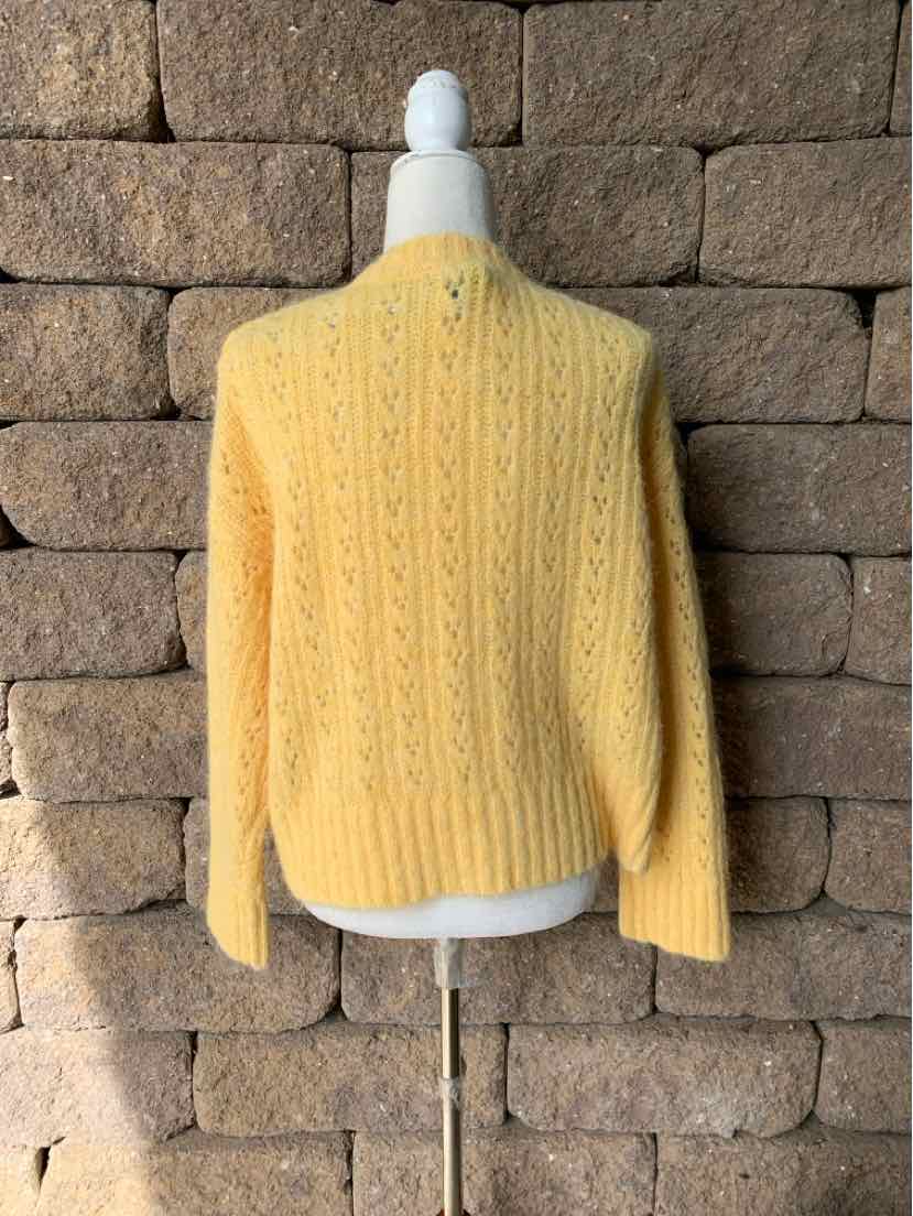 Yellow cable-knit sweater with a high ribbed neckline and long sleeves on a display form.