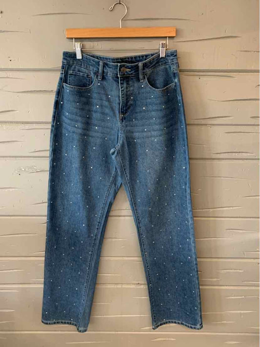 Blue denim jeans with a high waist and subtle white paint splatter details hanging on a wooden hanger.