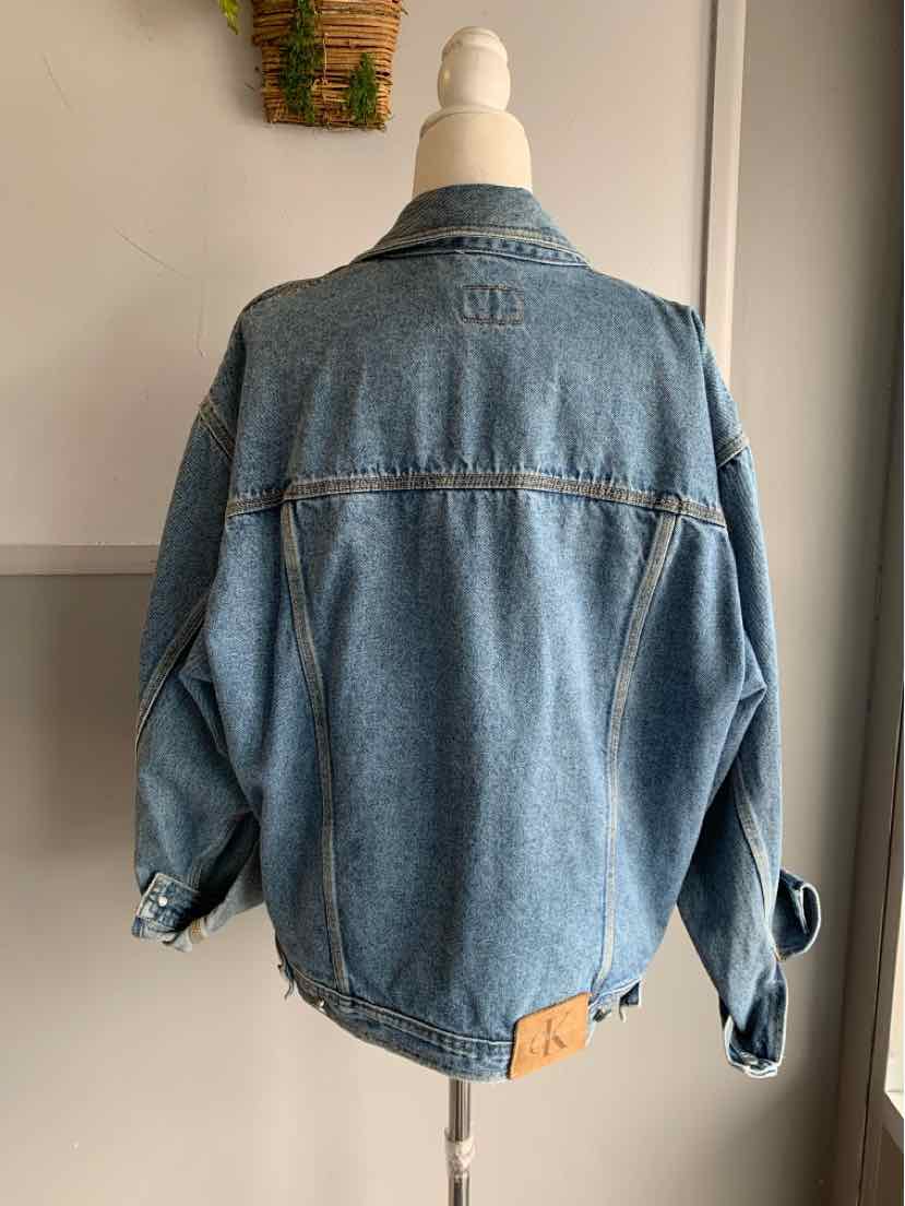 Light blue denim jacket with long sleeves, frayed cuffs, and a brown leather patch near the hem.