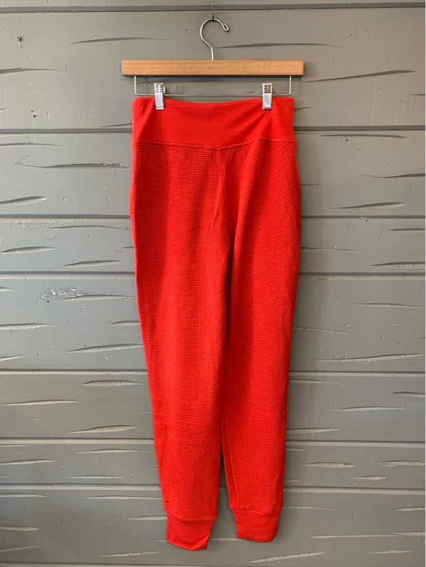 Bright red waffle-knit athletic leggings with a wide waistband and tapered ankles, hanging from a wooden clip hanger.