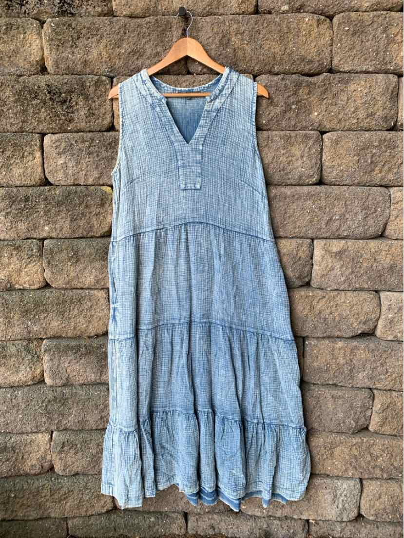 Sleeveless chambray blue midi dress with tiered skirt and V-neckline on wooden hanger.