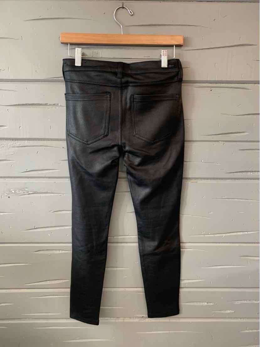 Black fitted pants with back pockets hanging on wooden hanger against gray wooden wall.