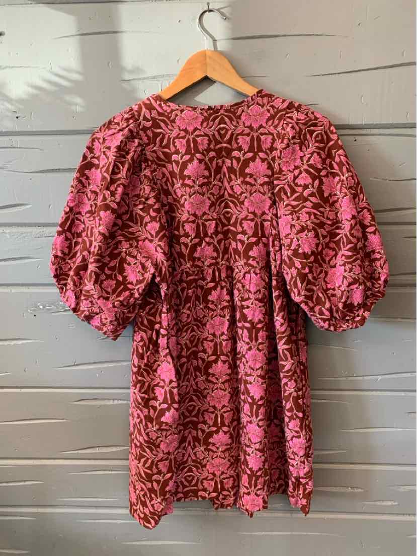 Pink floral dress with puff sleeves and loose fit on wooden hanger against gray wood panel background.