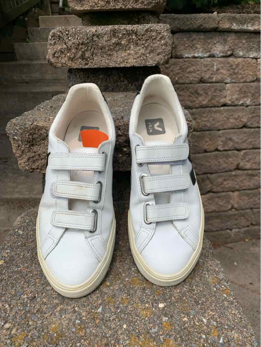White low-top sneakers with three adjustable Velcro straps, beige rubber soles, and subtle gray detailing on the sides.
