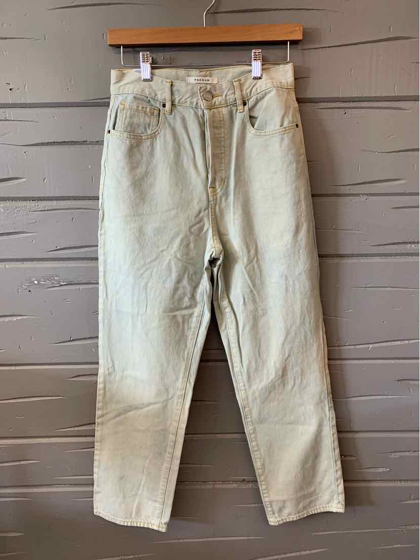 Light beige high-waisted denim jeans with five-pocket design hanging on wooden hanger against wooden wall.