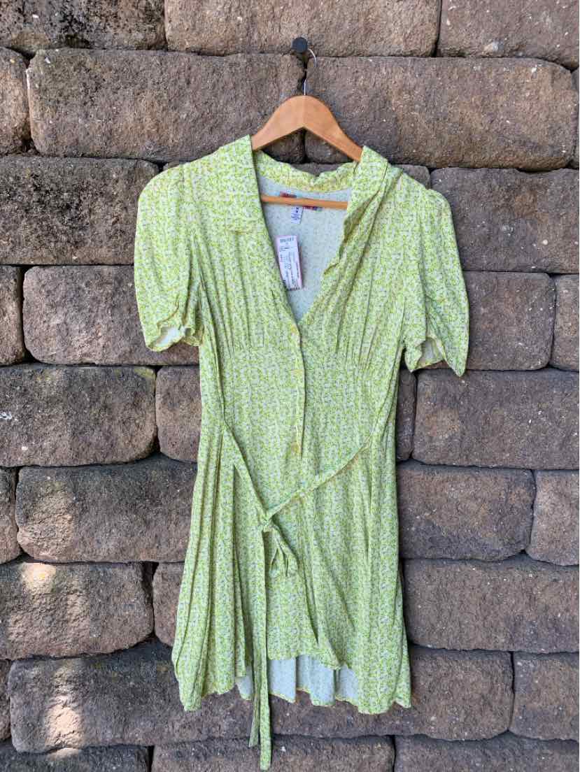 Light green floral wrap dress with short puff sleeves and v-neck collar hanging on wooden hanger.