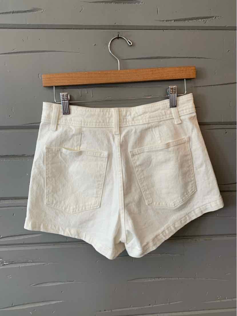 High-waisted white denim shorts with two back patch pockets and belt loops on a wooden hanger.
