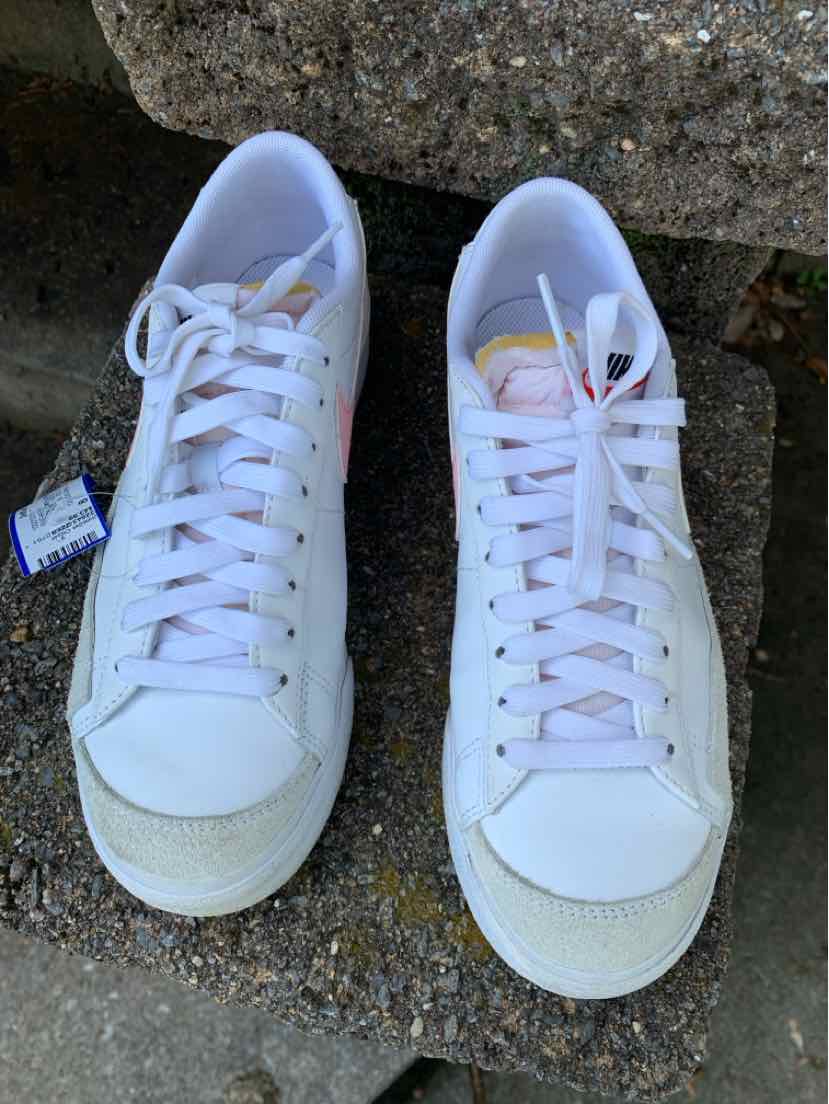 Pair of white Nike low-top sneakers with white laces, perforated toe caps, and subtle pastel accents.