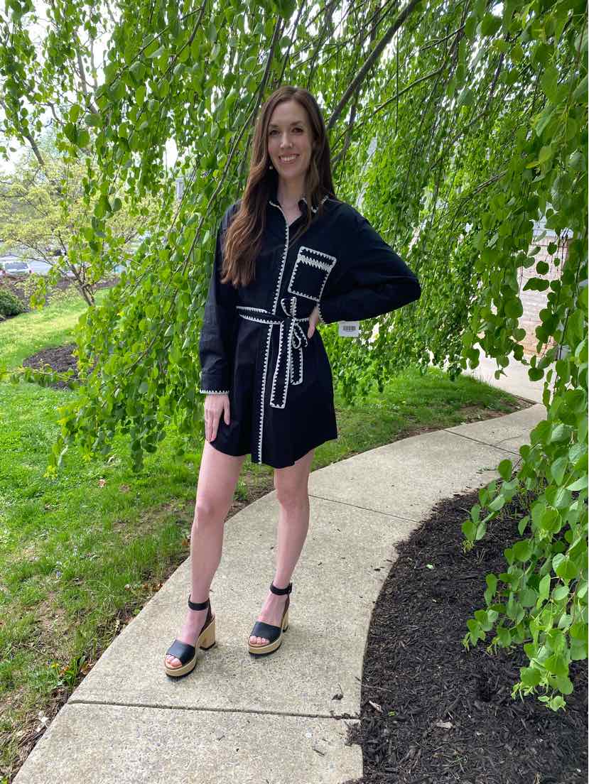 Black short dress with white piping, long sleeves, collar, and front tie belt, worn with black platform sandals.