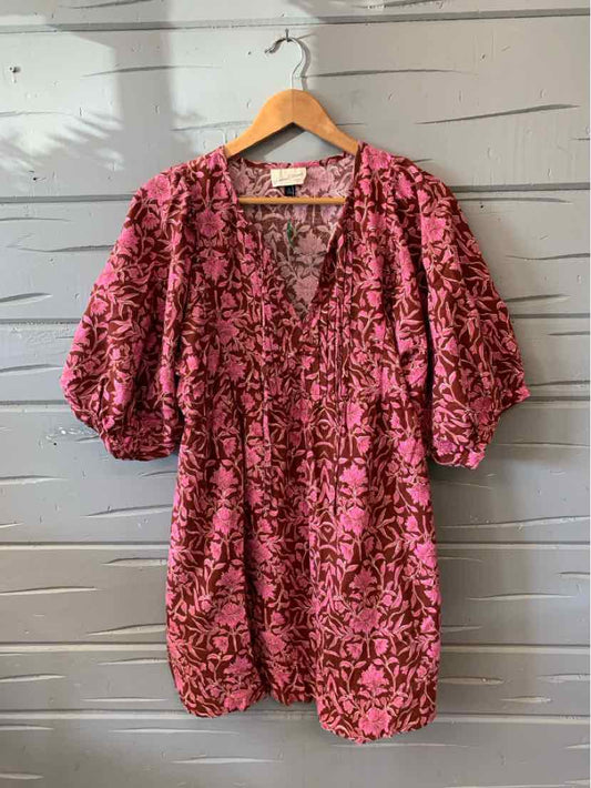 Pink floral short-sleeve romper with V-neck and cinched waist on wooden hanger.