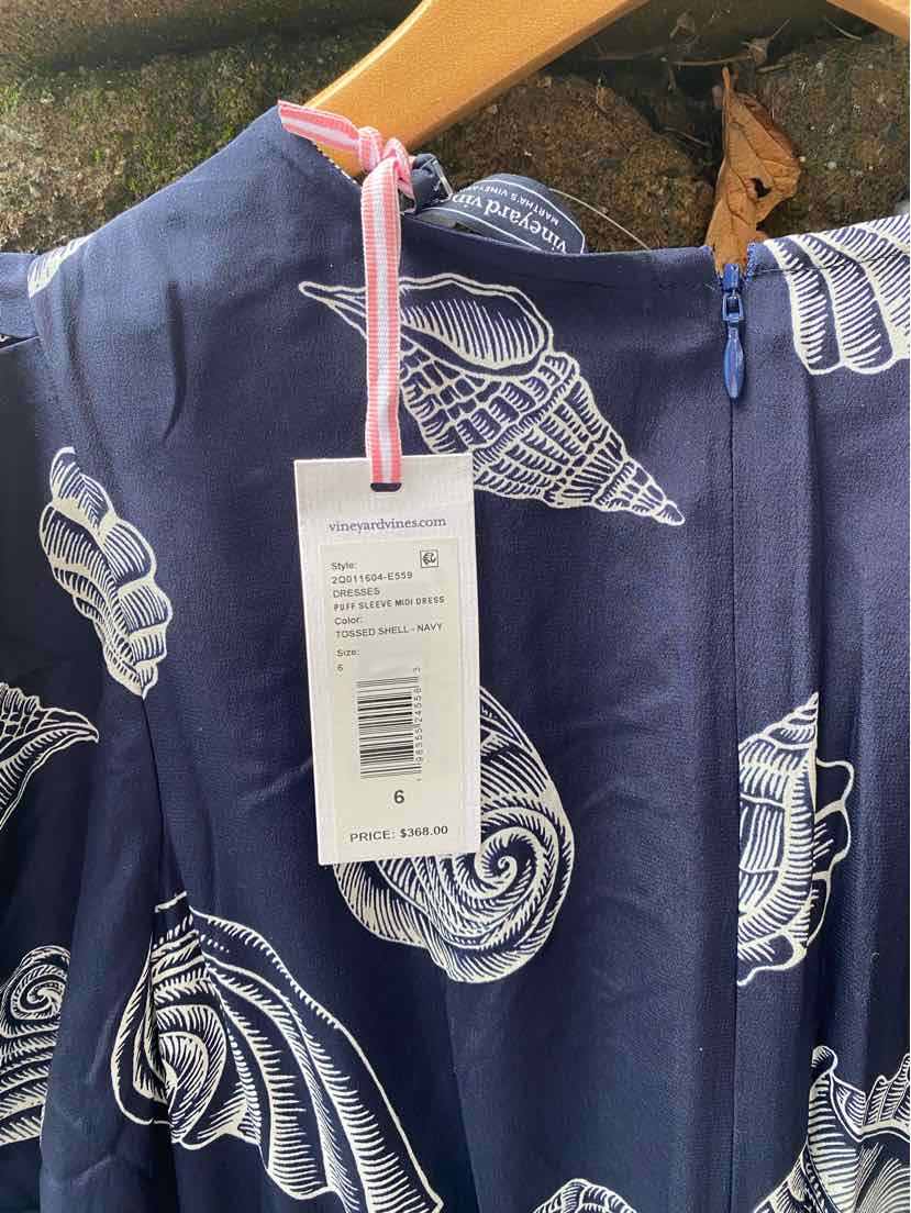 Navy blue dress with white seashell print and pink tag hanging on wooden hanger.
