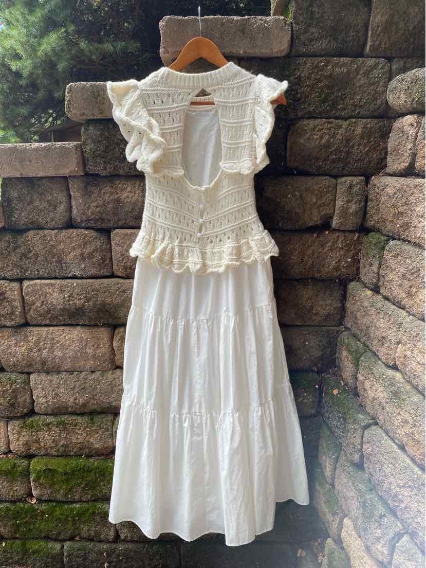 Cream-colored sleeveless knit top with ruffle details and keyhole back paired with long white tiered skirt.
