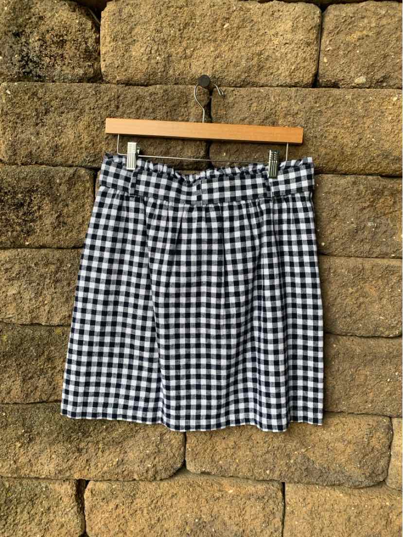 Black and white gingham patterned skirt with pleats, mid-length, hanging on wooden hanger.