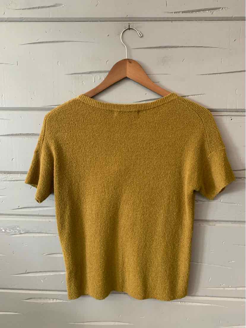 Mustard yellow short-sleeve knit top with subtle texture and a relaxed fit hanging on wooden hanger.