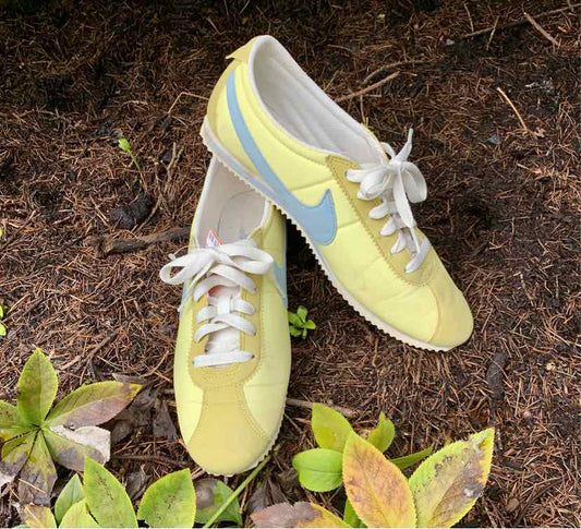 Yellow Nike sneakers with light blue swoosh, white laces, and low-top design on soil background.