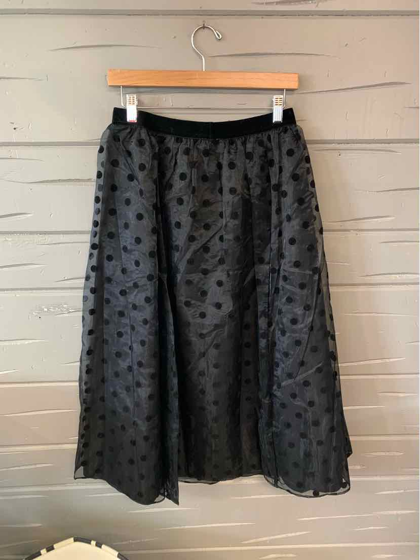 Black midi skirt with polka dot texture and elastic waistband hanging on wooden hanger.