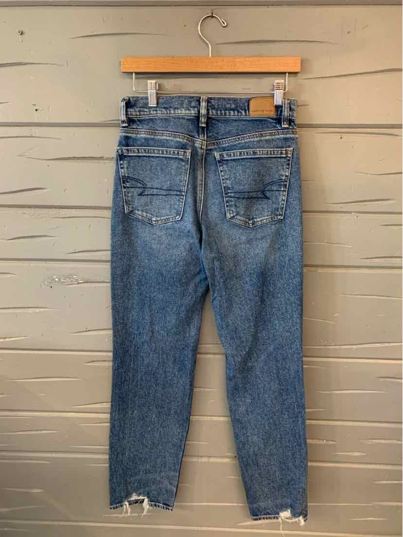 High-waisted blue denim jeans with a straight leg and frayed hems hanging on a wooden hanger, back view.