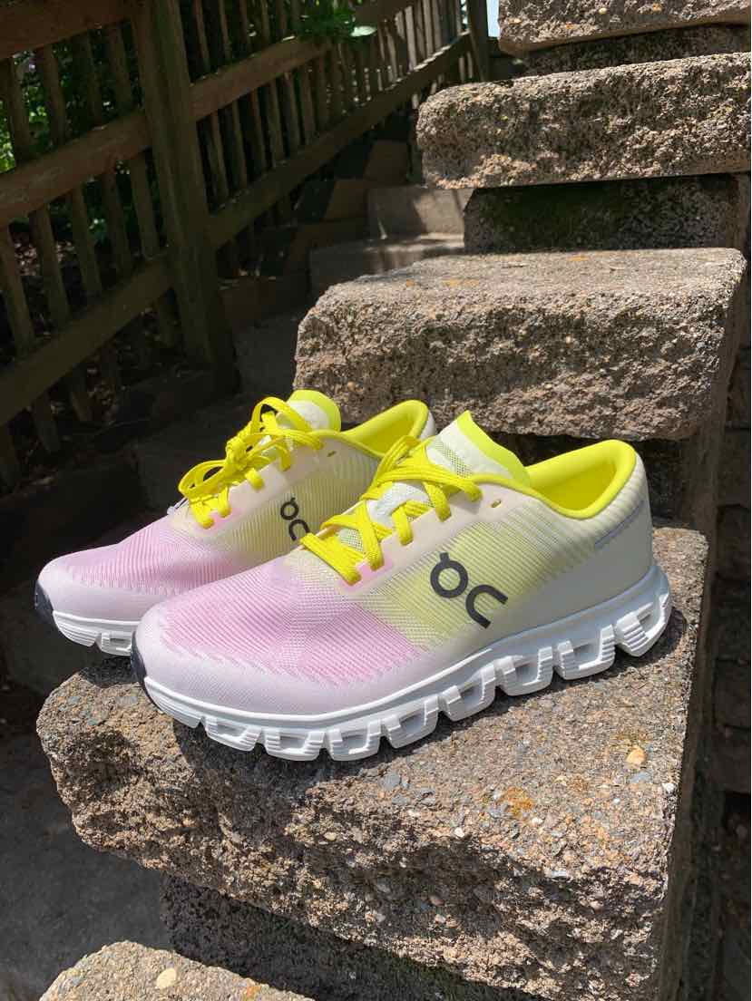 White and light pink low-top sneakers with yellow laces and cushioning soles featuring cloud-like pods.