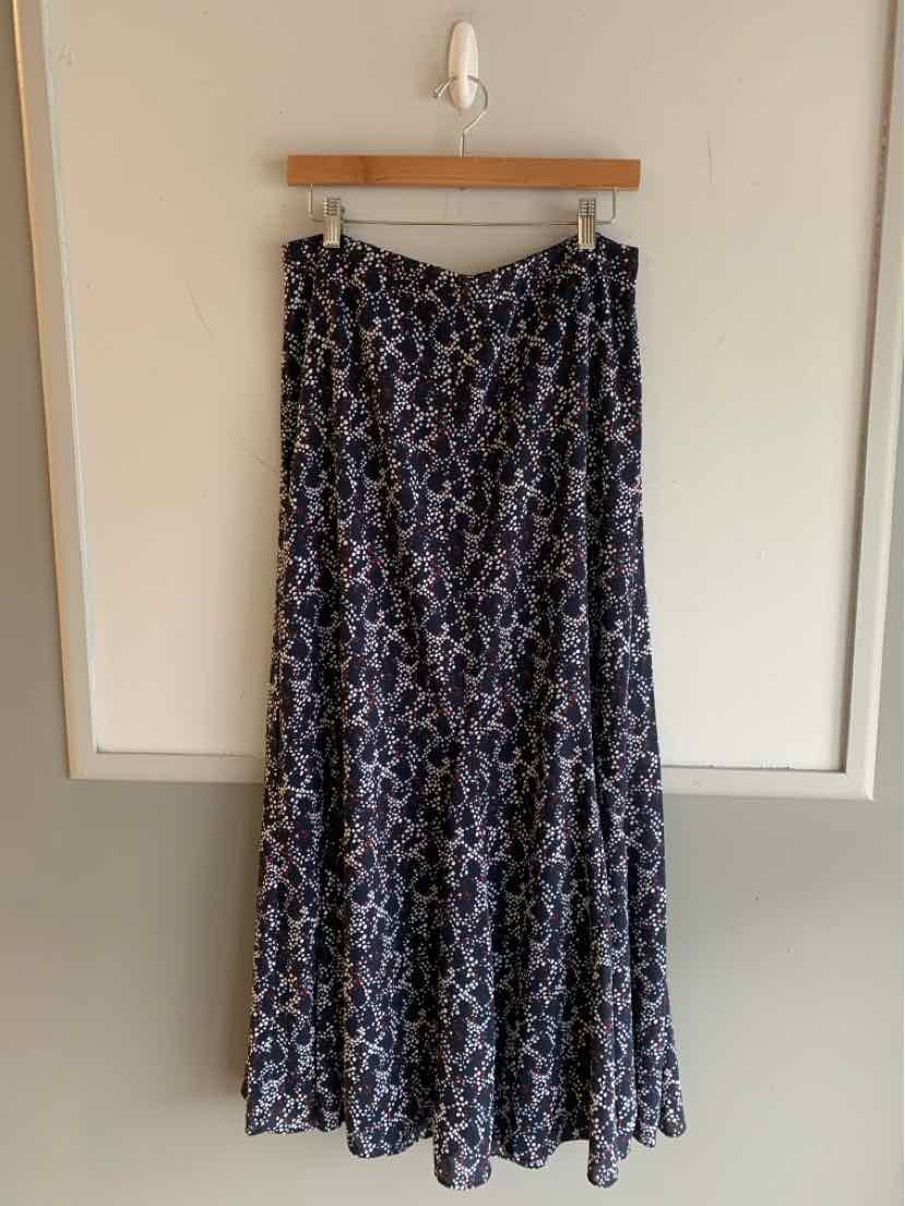 Black and white polka dot maxi skirt with flowy fabric and tiered hem hanging on wooden hanger.