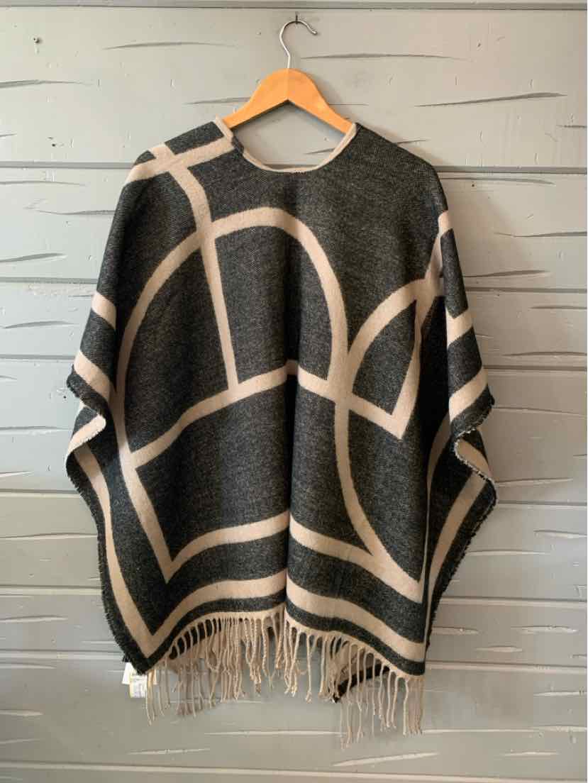 Dark gray poncho with wide beige geometric lines and fringed hem hanging on wooden hanger.